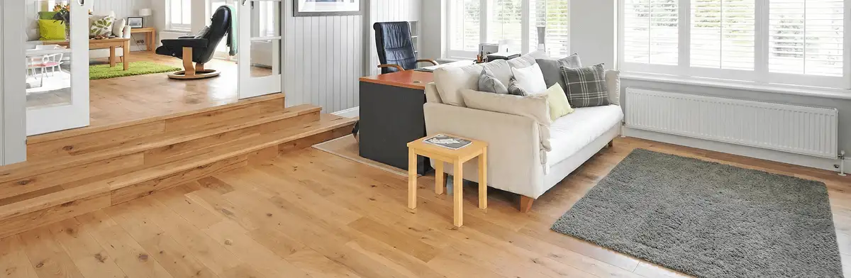 A modern living room with professionally installed laminate flooring, a beige sofa, a small side table, a gray rug, and large windows with white shutters in Naperville, IL